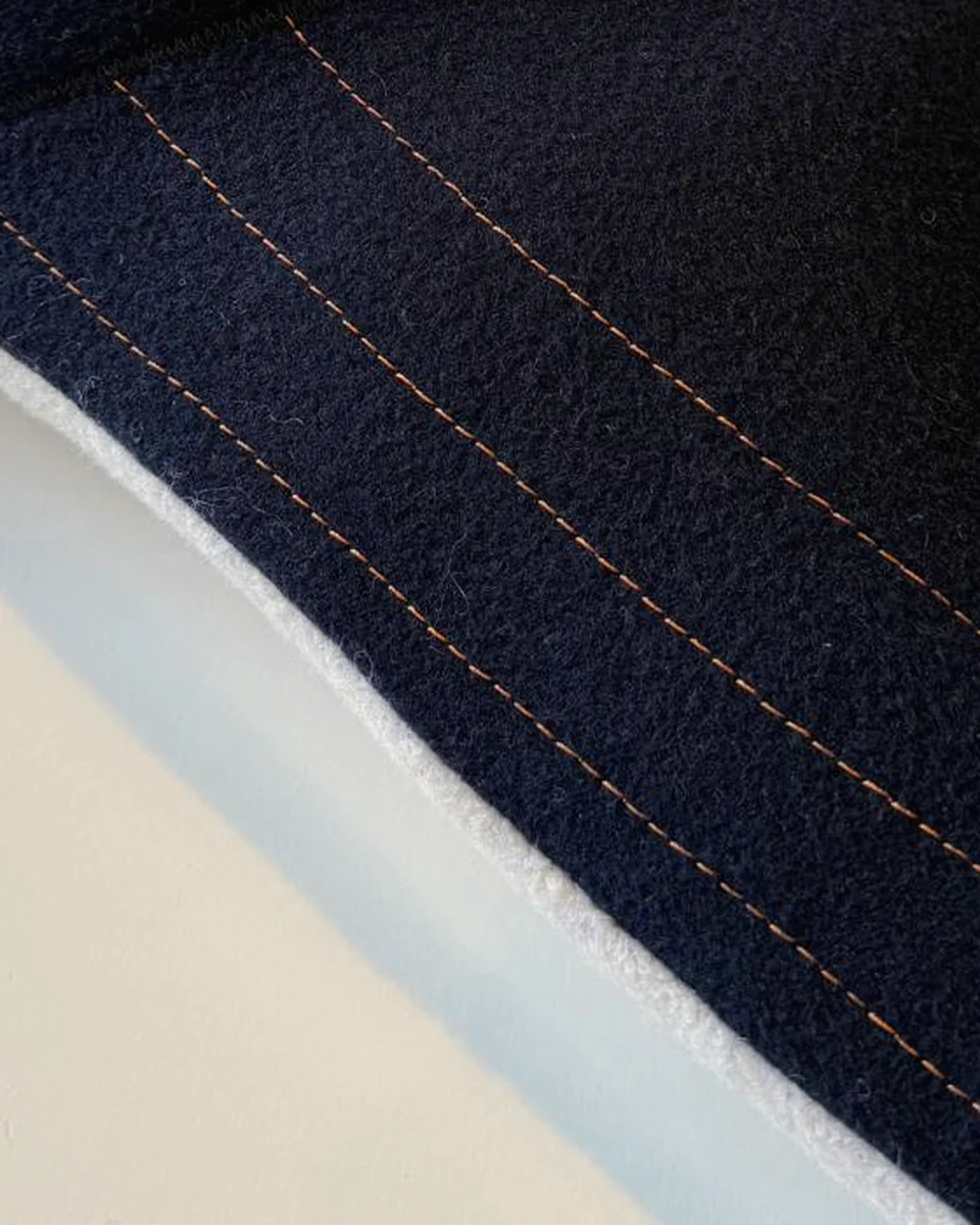 Close view of Cove's navy wool, three copper stitch lines and the cream underside edge